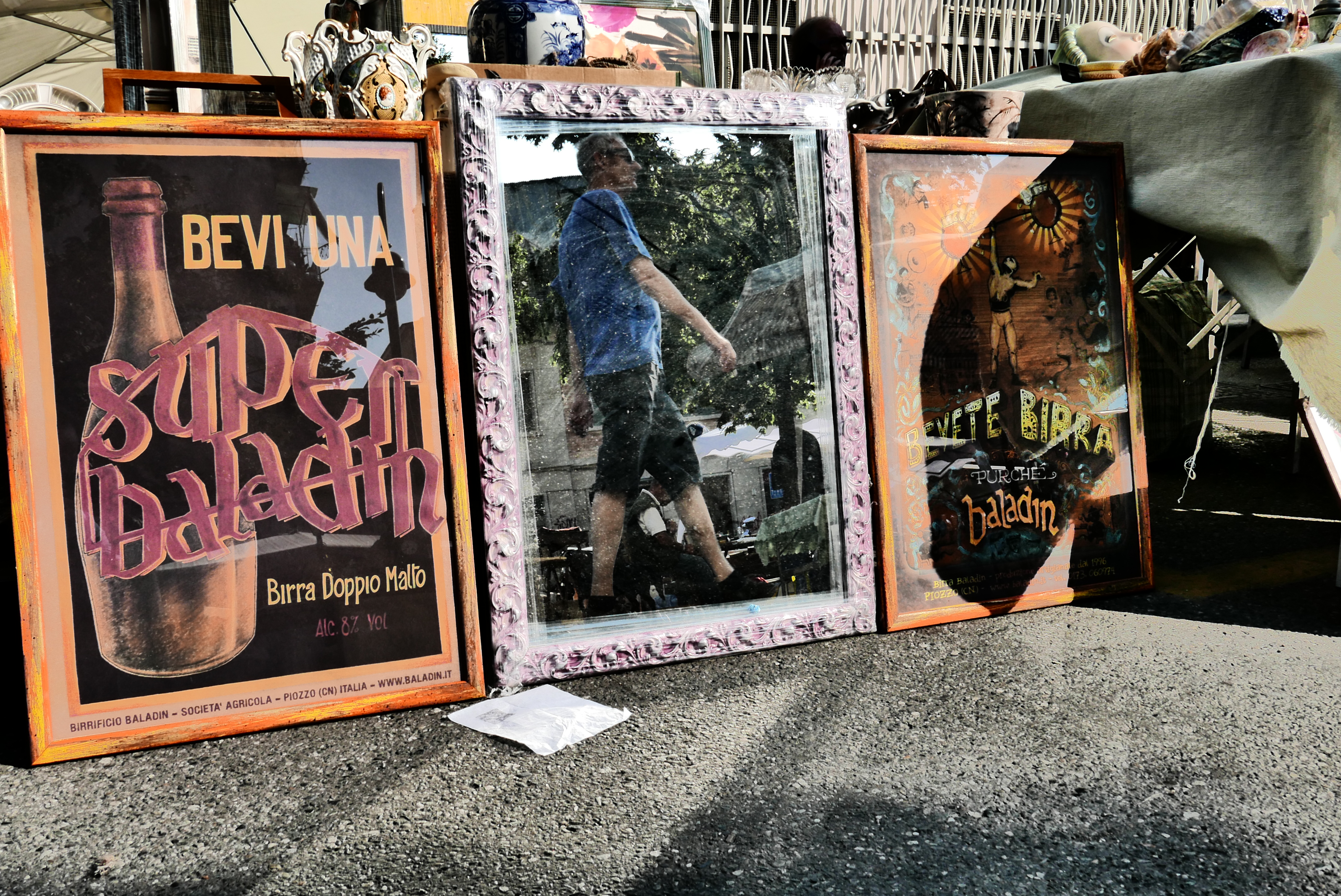 tre quadri, quello centrale è uno specchio che riflette una persona che cammina. gli altri due sono cartelloni pubblicitari della birra.