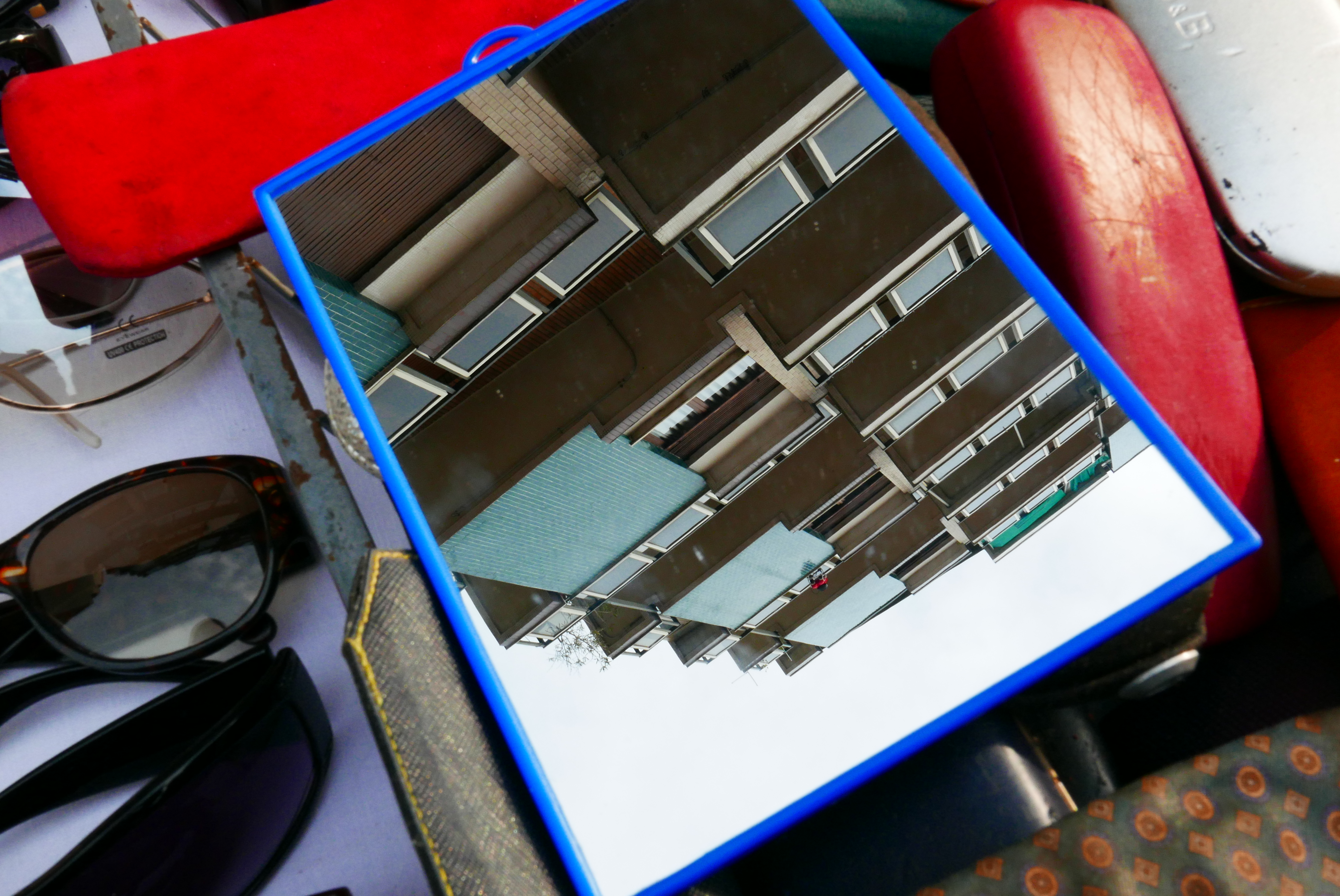 uno specchio con cornice blu appoggiato su una bancarella riflette un palazzo.