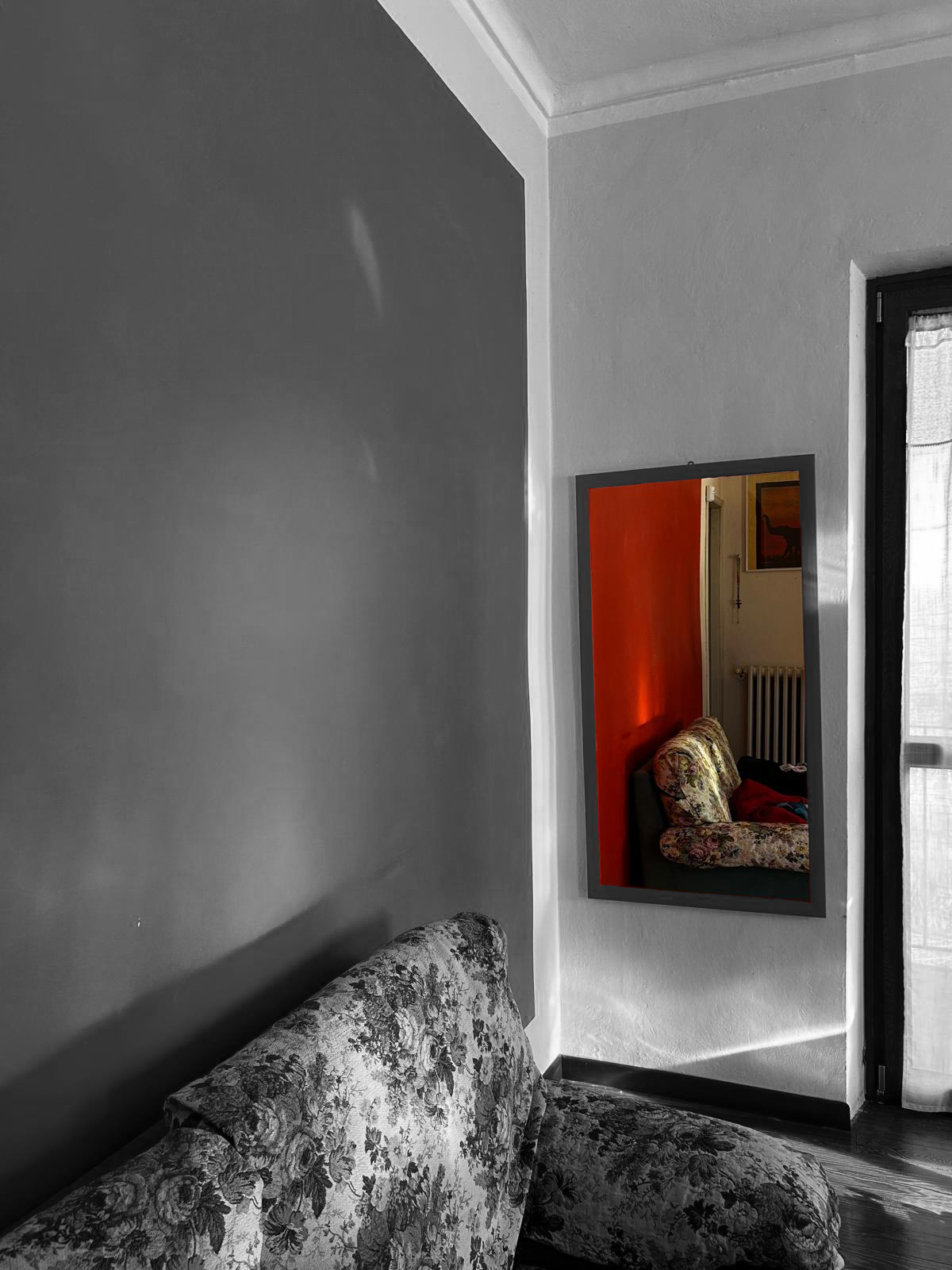 Uno specchio riflette parte della stanza e del divano, nel riflesso è a colori mentre il resto è in bianco e nero.