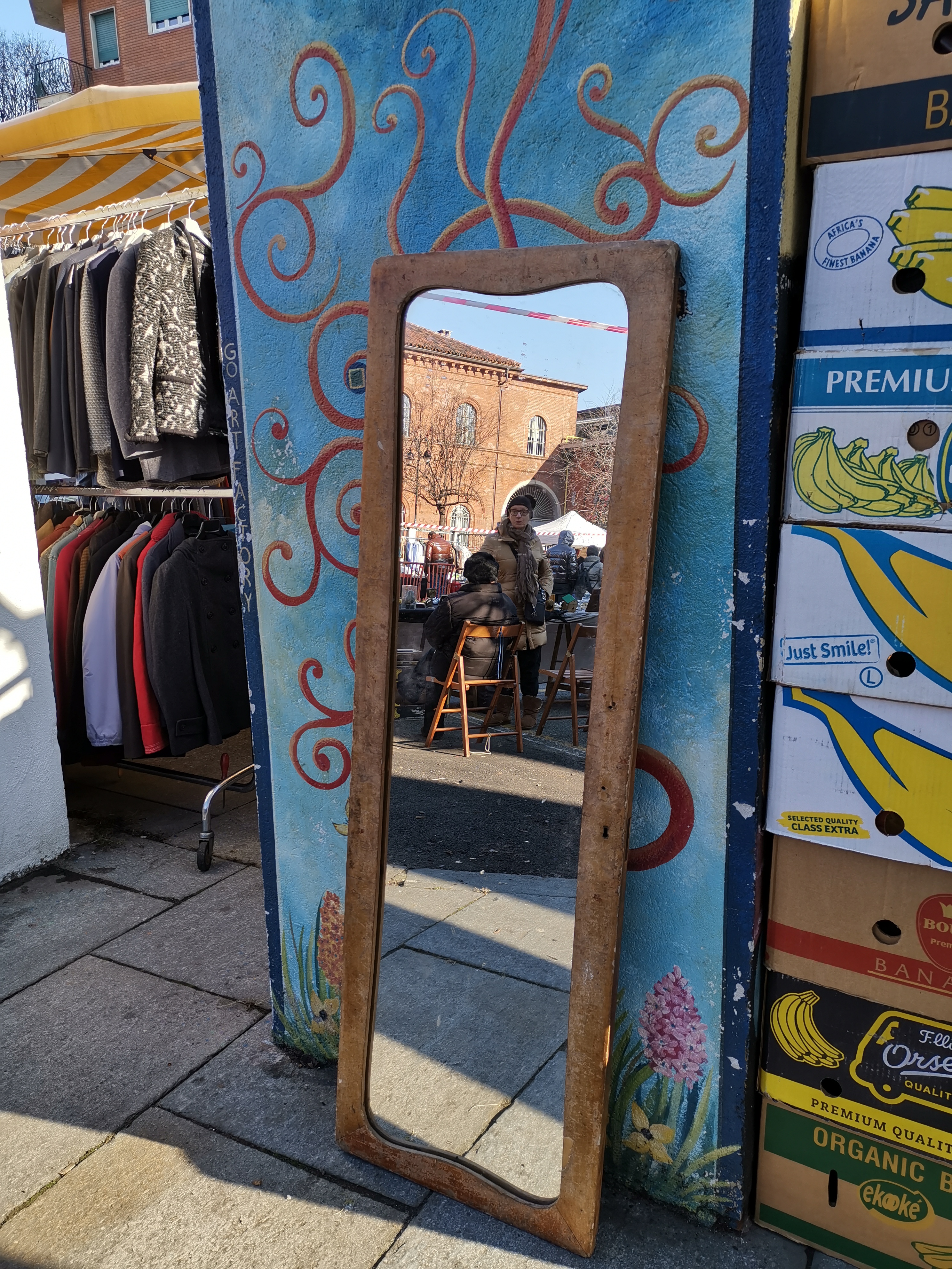 Uno specchio appoggiato ad un muro riflette due mercanti di antiquariato e la loro bancarella.